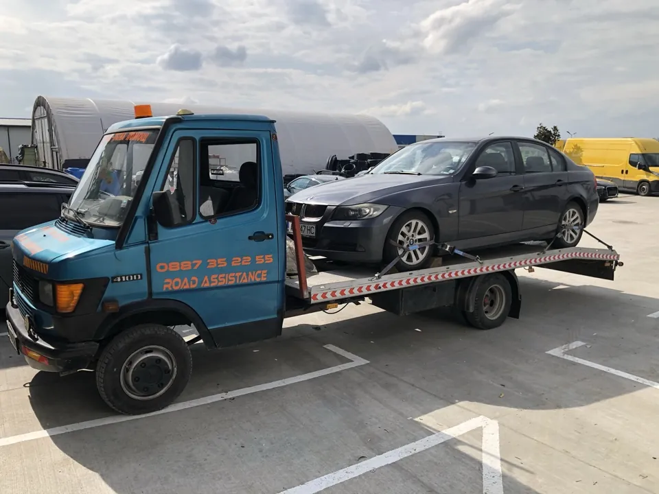 Син платформен пътен влекач ROAD Assistance с натоварен сив BMW седан на платформата, пътна помощ в Бургас