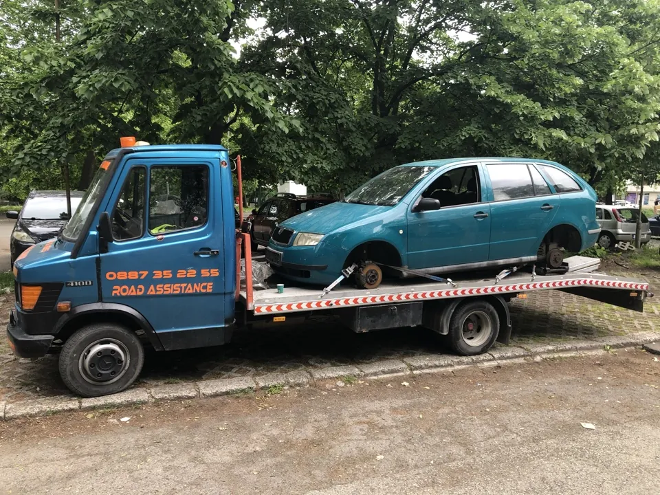 Син платформен автомобил за пътна помощ в Бургас с надпис ROAD ASSISTANCE, натоварен със зелено комби с демонтирани предни гуми