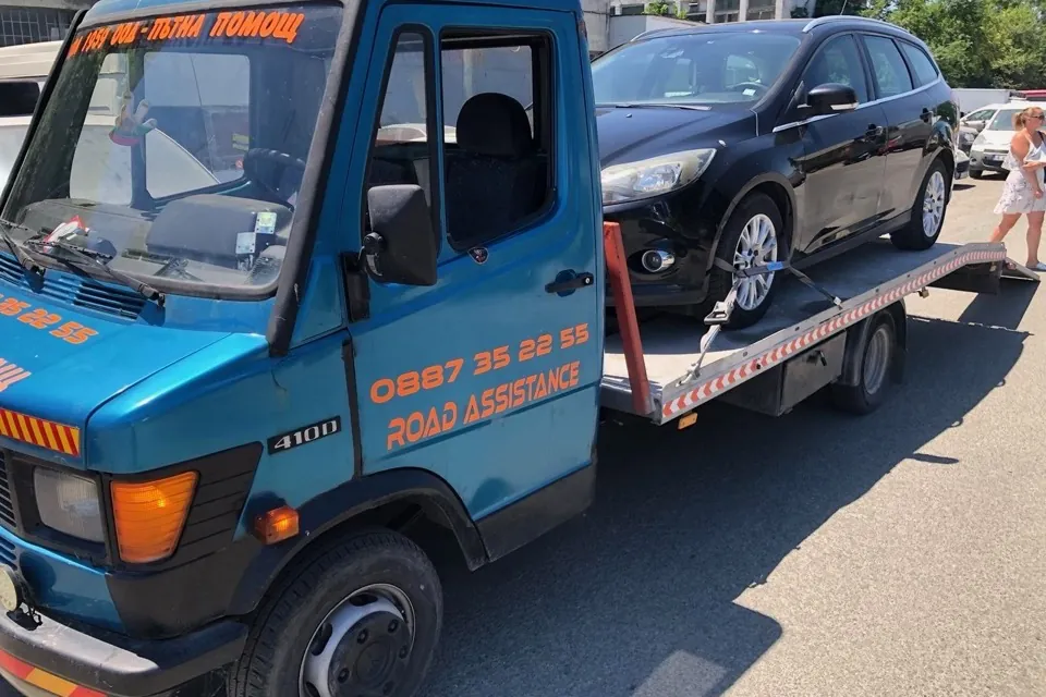 Син платформен влекач ROAD Assistance с натоварено черно комби Ford — пътна помощ в Бургас